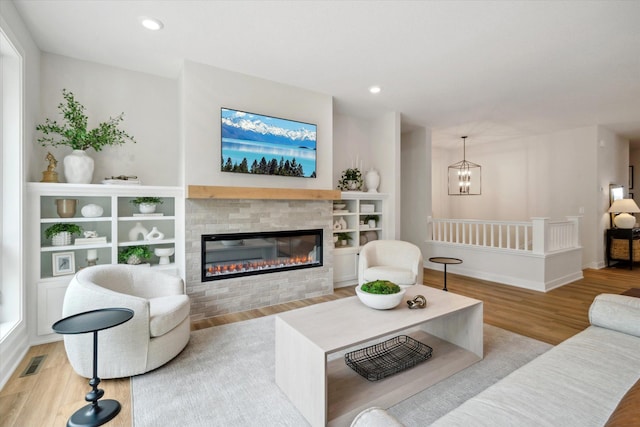 living room featuring a tiled fireplace, an inviting chandelier, and light wood-type flooring