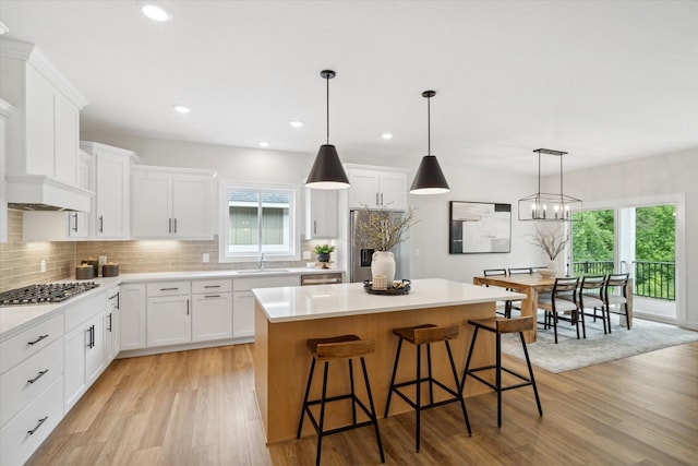 kitchen with white cabinets, a kitchen island, pendant lighting, and light hardwood / wood-style flooring