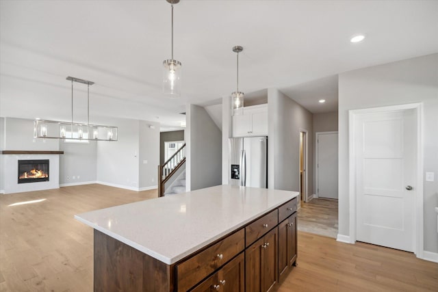 kitchen with a center island, white cabinets, stainless steel refrigerator with ice dispenser, hanging light fixtures, and light hardwood / wood-style flooring