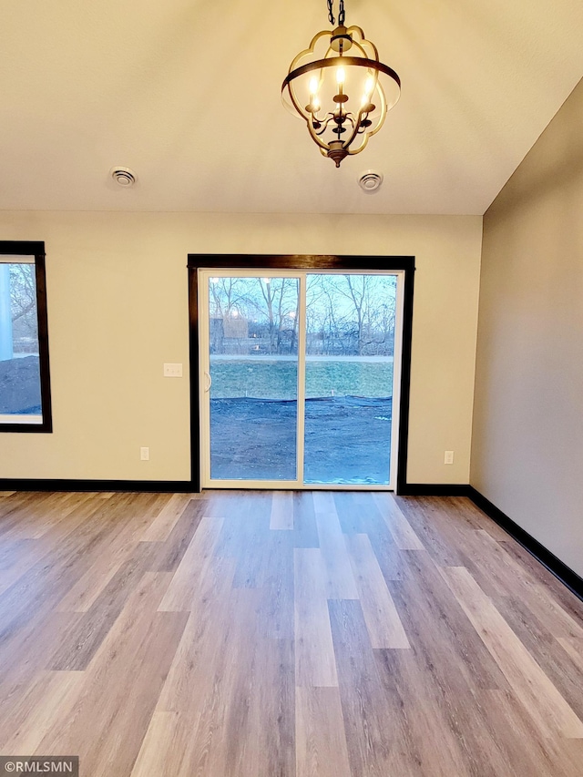 empty room featuring a notable chandelier and light hardwood / wood-style flooring