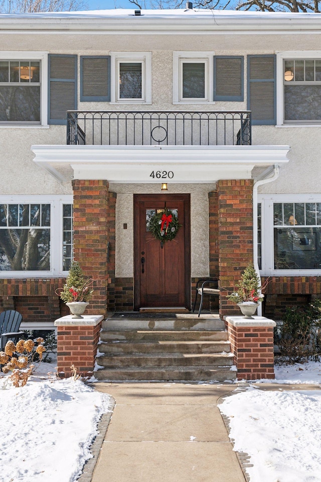 snow covered property entrance with a balcony and covered porch