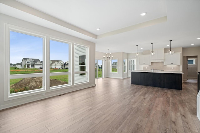 kitchen with a wealth of natural light, light wood-type flooring, white cabinetry, and a kitchen island with sink