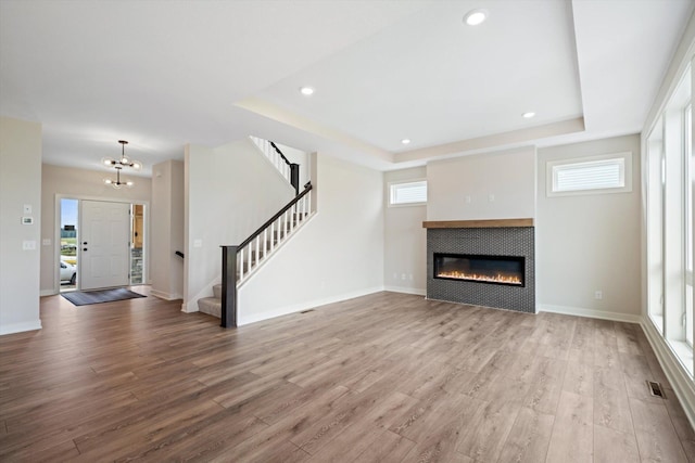 unfurnished living room with a tile fireplace, wood-type flooring, a tray ceiling, and a chandelier