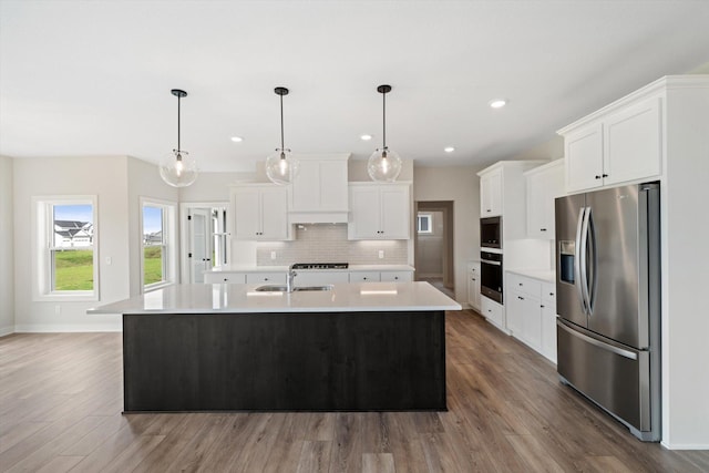 kitchen featuring hardwood / wood-style floors, stainless steel appliances, pendant lighting, and an island with sink