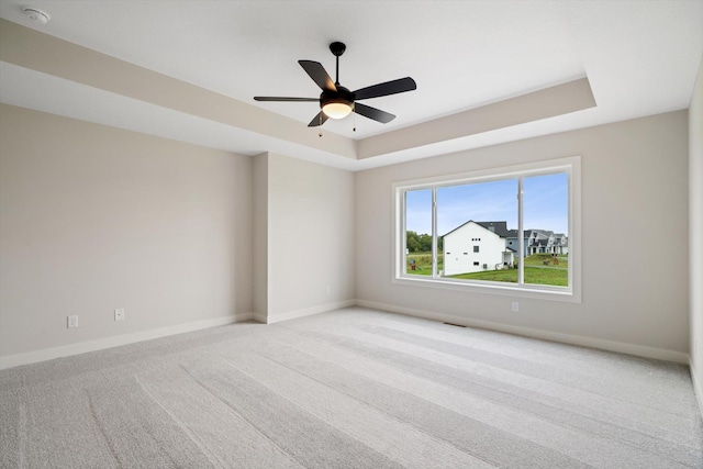 unfurnished room featuring ceiling fan, a raised ceiling, and light carpet