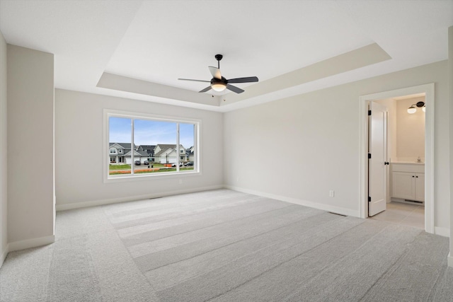 carpeted empty room with a raised ceiling and ceiling fan