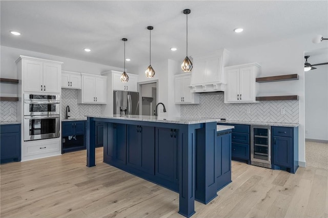 kitchen featuring blue cabinets, hanging light fixtures, white cabinetry, stainless steel appliances, and beverage cooler