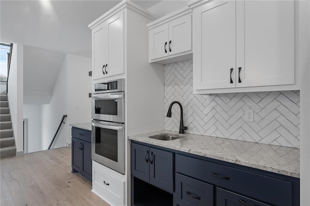 kitchen with light wood-type flooring, light stone counters, double oven, sink, and white cabinets