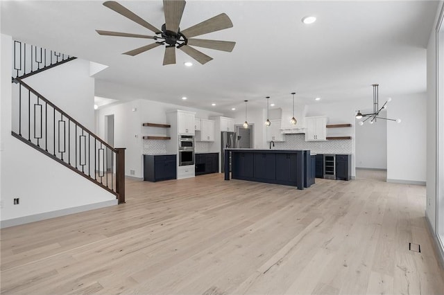 unfurnished living room with ceiling fan with notable chandelier, light hardwood / wood-style floors, and sink