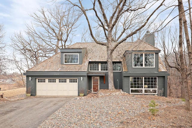 view of front facade featuring a chimney, driveway, and an attached garage