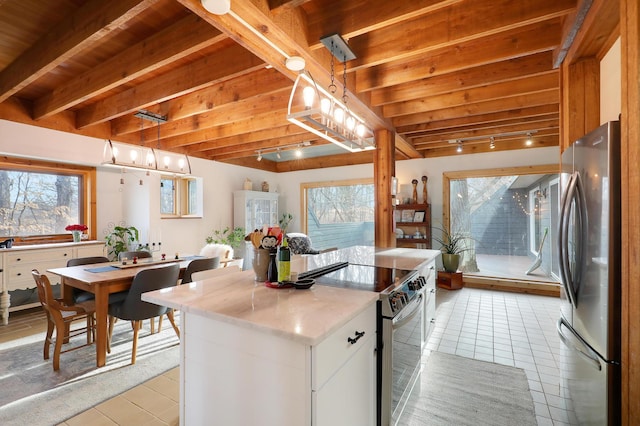 kitchen with beam ceiling, light tile patterned flooring, appliances with stainless steel finishes, and a kitchen island