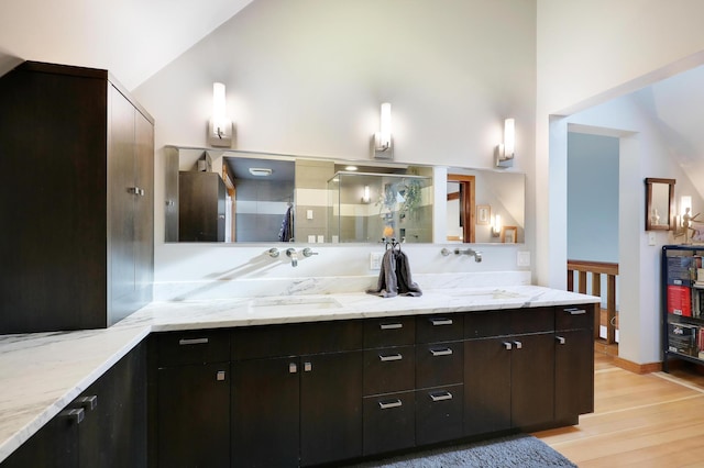 bathroom with wood finished floors, high vaulted ceiling, double vanity, a sink, and a shower stall