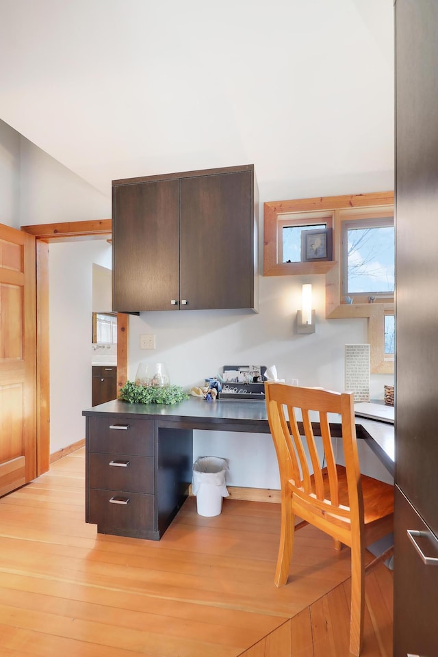 kitchen with dark brown cabinetry, light wood finished floors, and dark countertops