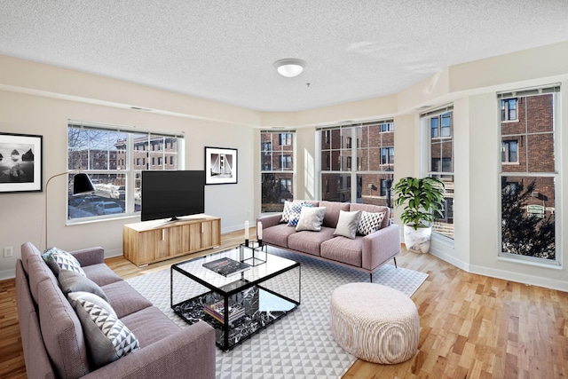 living room with a textured ceiling, light wood-type flooring, and baseboards