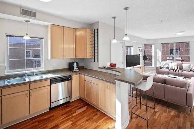 kitchen featuring dark countertops, stainless steel dishwasher, open floor plan, a sink, and a peninsula