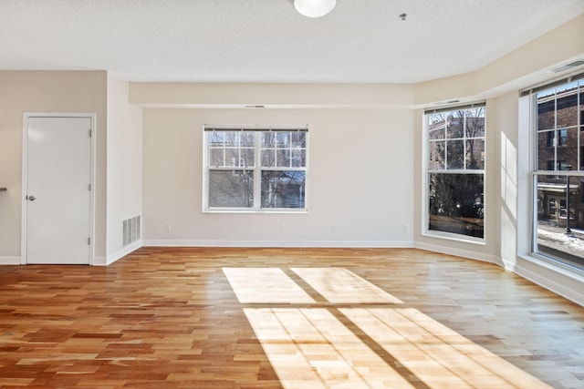 empty room featuring a textured ceiling, visible vents, and light wood-style floors