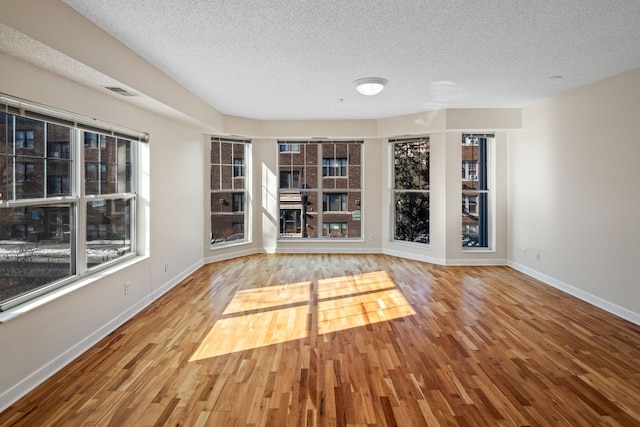 empty room with a textured ceiling, baseboards, wood finished floors, and visible vents