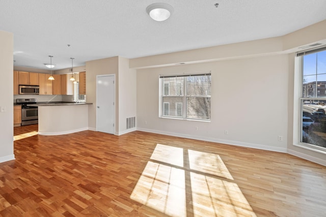 unfurnished living room with light wood-style floors, baseboards, and visible vents
