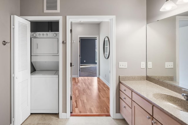 bathroom with vanity, stacked washing maching and dryer, baseboards, wood finished floors, and visible vents