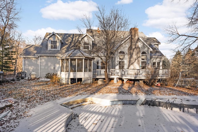 snow covered rear of property featuring a sunroom and a deck