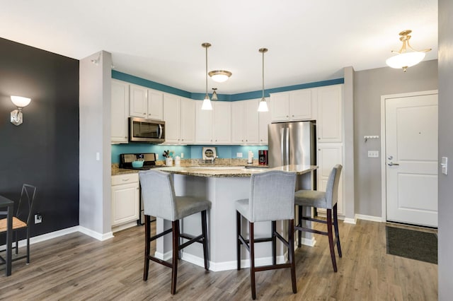 kitchen with white cabinetry, hanging light fixtures, stainless steel appliances, light hardwood / wood-style floors, and a kitchen island