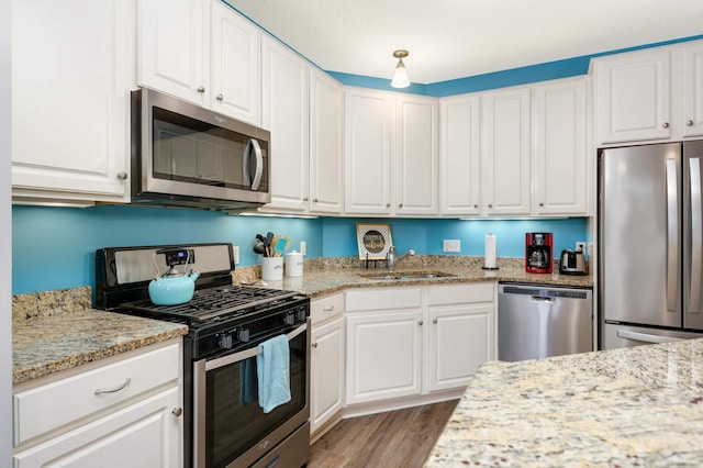 kitchen with light stone counters, stainless steel appliances, sink, light hardwood / wood-style flooring, and white cabinetry