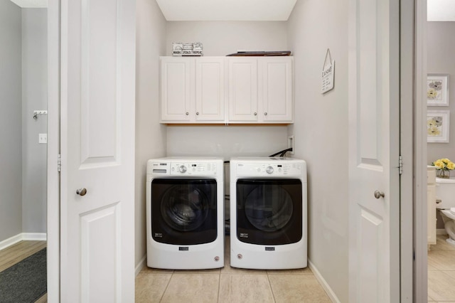 clothes washing area featuring cabinets, washing machine and dryer, and light tile patterned floors