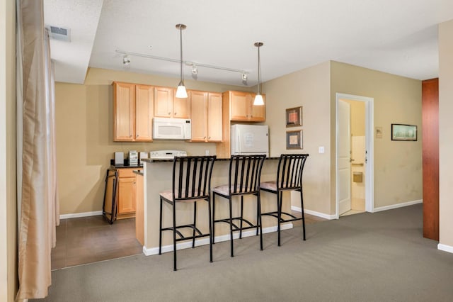 kitchen featuring dark carpet, white appliances, hanging light fixtures, light brown cabinetry, and a breakfast bar area