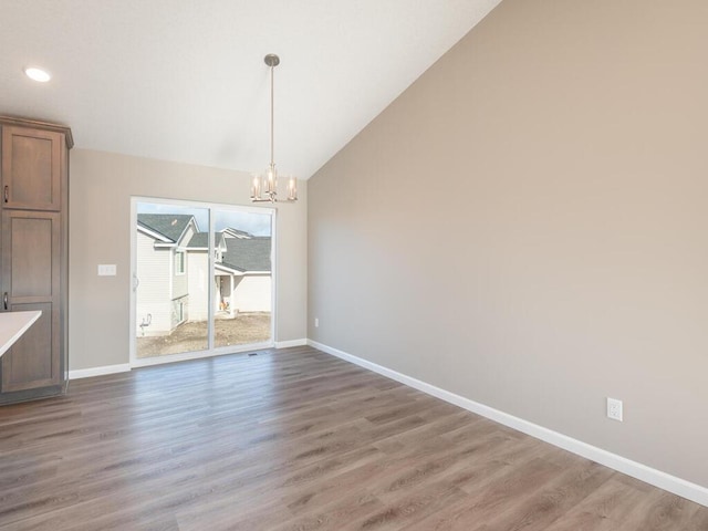 unfurnished dining area featuring wood-type flooring, lofted ceiling, and a notable chandelier