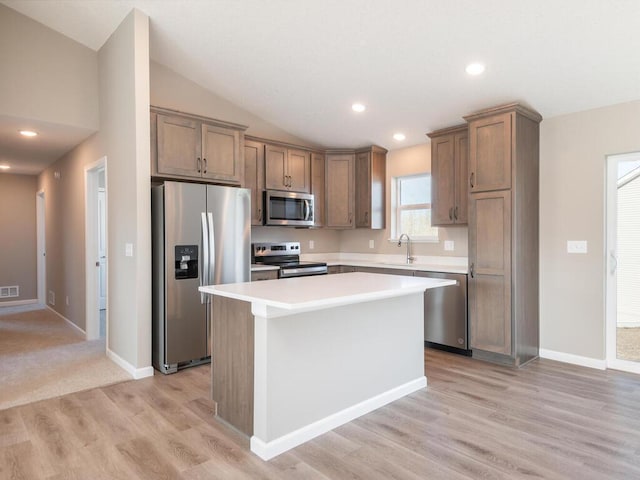 kitchen with appliances with stainless steel finishes, a center island, light hardwood / wood-style flooring, and vaulted ceiling