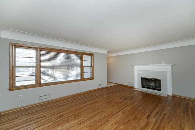 unfurnished living room featuring wood finished floors, plenty of natural light, a tile fireplace, and baseboards