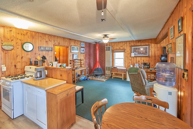 kitchen featuring a wood stove, white gas range, ceiling fan, a textured ceiling, and wooden walls