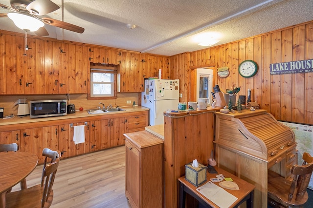 kitchen with sink, light hardwood / wood-style flooring, wood walls, white fridge, and a textured ceiling