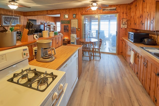 kitchen featuring sink, wooden walls, ceiling fan, light wood-type flooring, and white range with gas stovetop