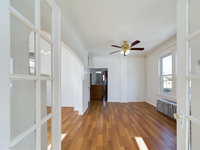 spare room with arched walkways, radiator, ceiling fan, dark wood-type flooring, and crown molding