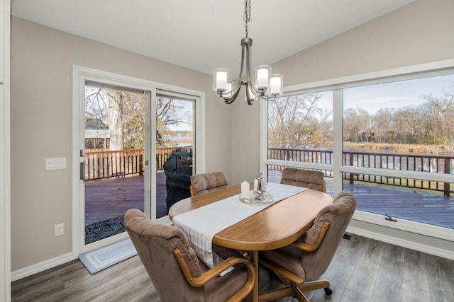 dining space with lofted ceiling, a wealth of natural light, wood-type flooring, and an inviting chandelier