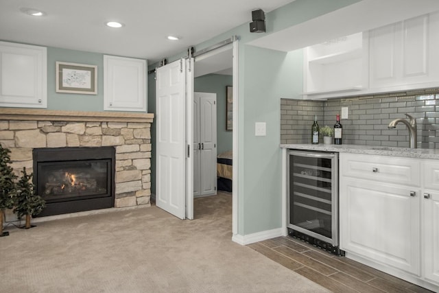 bar with tasteful backsplash, white cabinetry, sink, wine cooler, and a barn door