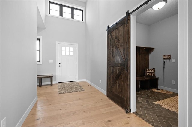 entryway with a towering ceiling, a barn door, light hardwood / wood-style floors, and a healthy amount of sunlight