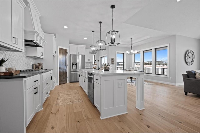 kitchen with appliances with stainless steel finishes, light hardwood / wood-style floors, white cabinetry, hanging light fixtures, and an island with sink