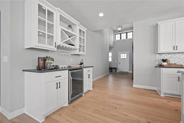 kitchen with light wood-type flooring, white cabinetry, a textured ceiling, and wine cooler