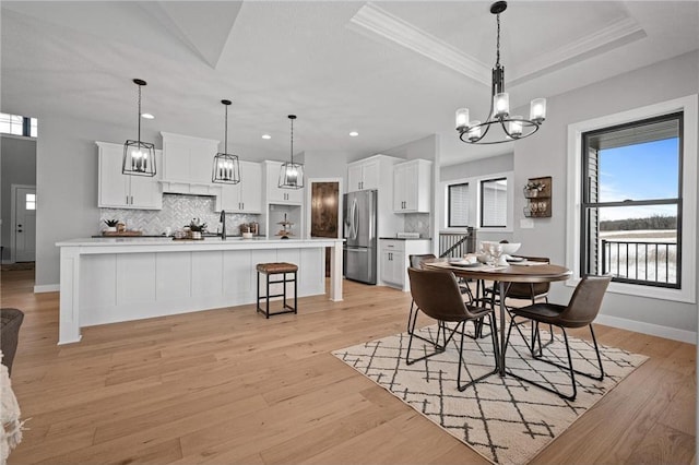 dining area with a tray ceiling, crown molding, and light hardwood / wood-style flooring