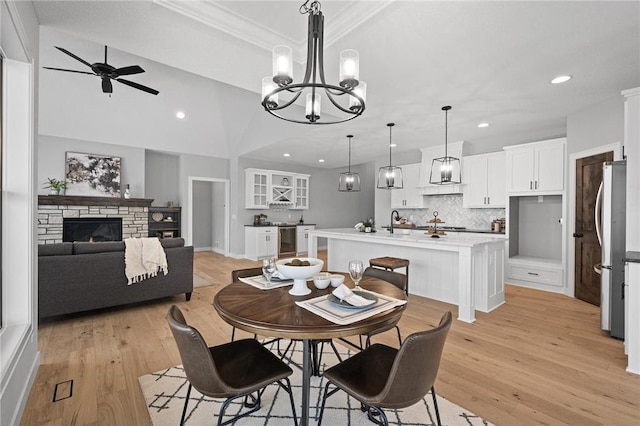 dining space featuring sink, a stone fireplace, light hardwood / wood-style floors, lofted ceiling, and ceiling fan with notable chandelier