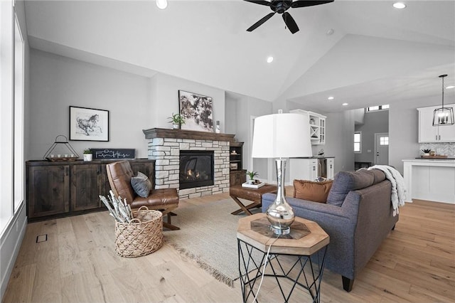 living room with ceiling fan, light wood-type flooring, a fireplace, and high vaulted ceiling