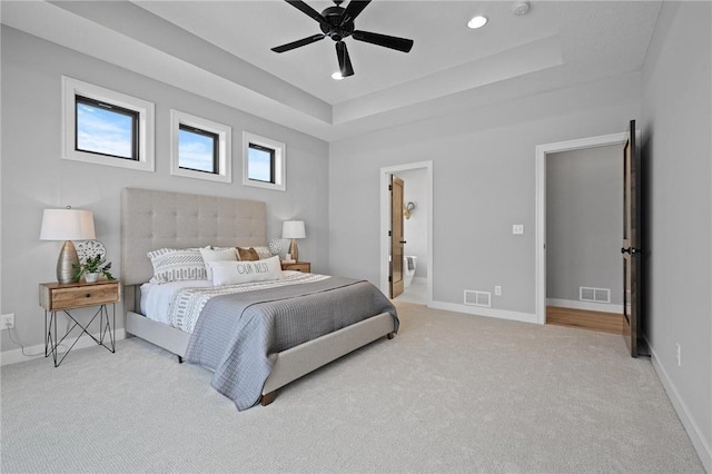 carpeted bedroom with a tray ceiling, ensuite bath, and ceiling fan