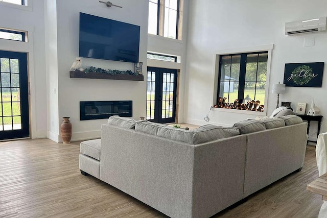 living room featuring a wall unit AC, french doors, wood-type flooring, and a high ceiling