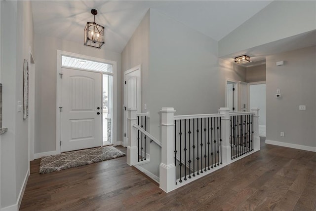 entryway with dark wood-type flooring, vaulted ceiling, and an inviting chandelier