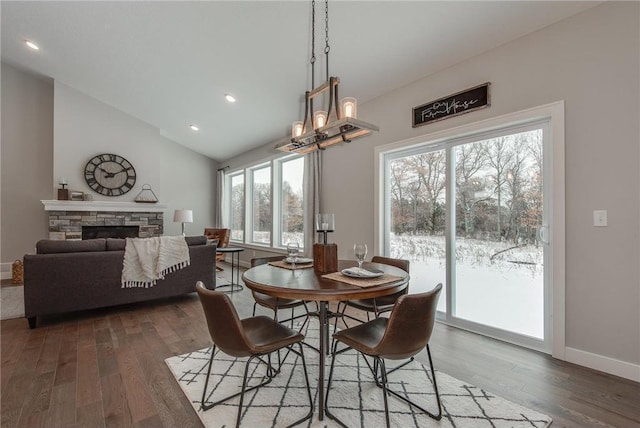 dining room with dark hardwood / wood-style flooring, a stone fireplace, a wealth of natural light, and vaulted ceiling