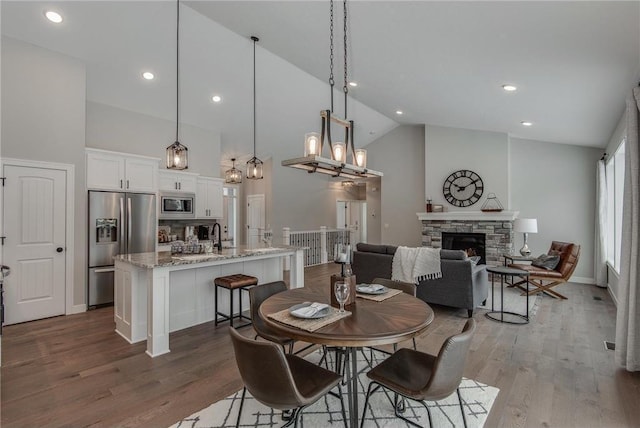 dining area with a stone fireplace, high vaulted ceiling, and wood-type flooring