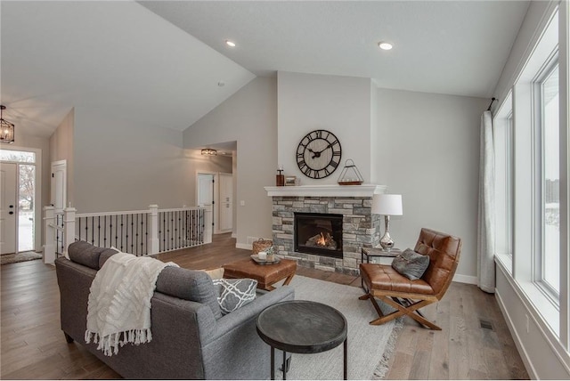 living room featuring a stone fireplace, a wealth of natural light, high vaulted ceiling, and wood-type flooring