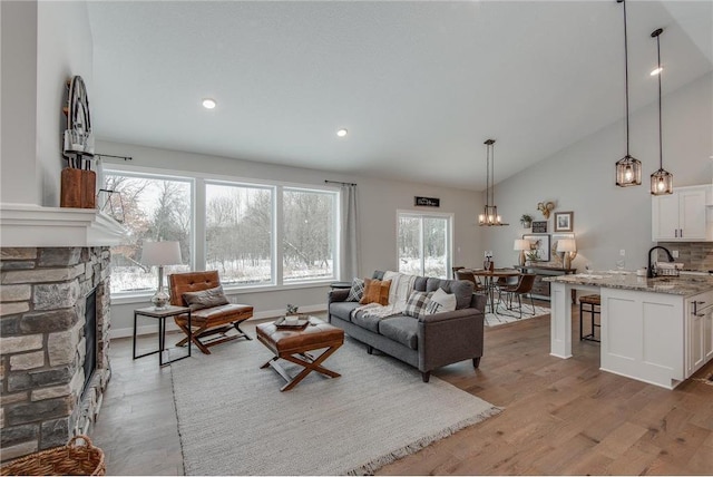 living room with hardwood / wood-style flooring, a stone fireplace, lofted ceiling, and sink